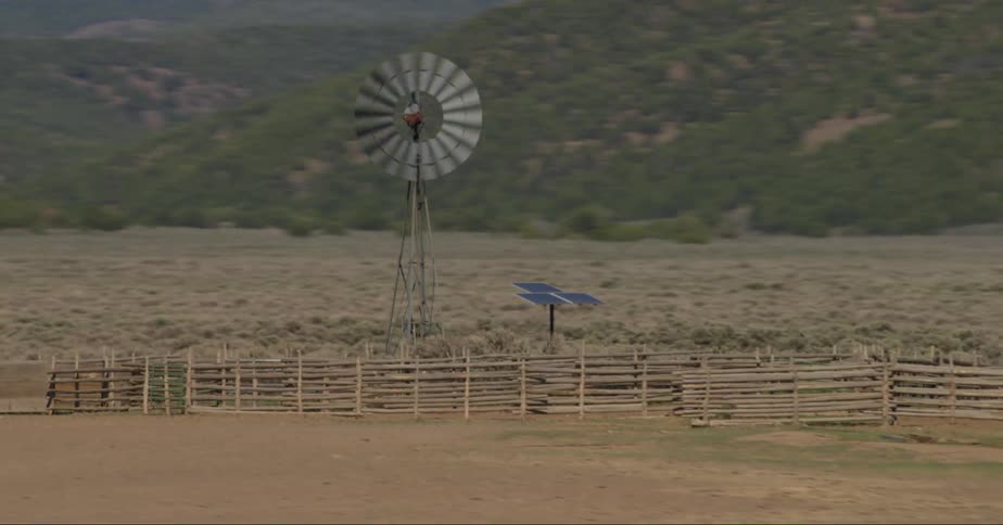 A windmill in a field behind a fence connected to solar panels