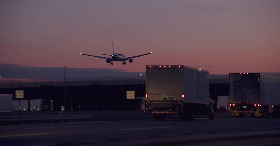 Airliner landing on a runway next to a busy highway at evening