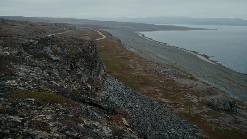 Person jumps off promontory and paraglides onto beach on misty day