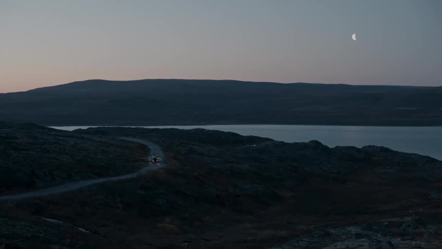 Car drives on a road near a lake while the moon rises at nightfall