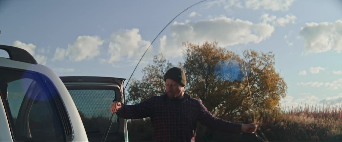 Man with beanie beard plaid shirt and pants puts fishing rod in car