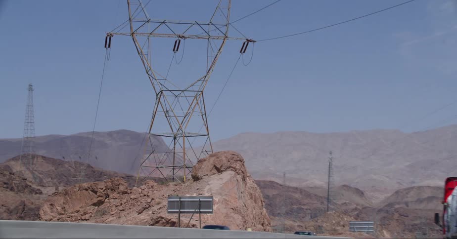 View of electricity transmission towers on rocky peaks next to a road