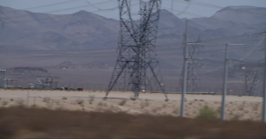 Utility towers and cables stretch across the desert with mountains in the distance