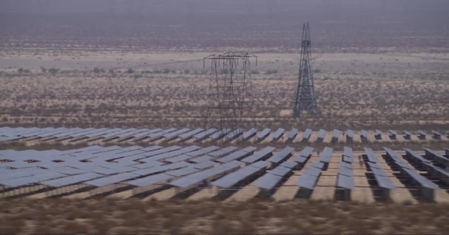 An aerial view of power towers surrounded by solar panels in an open desert field