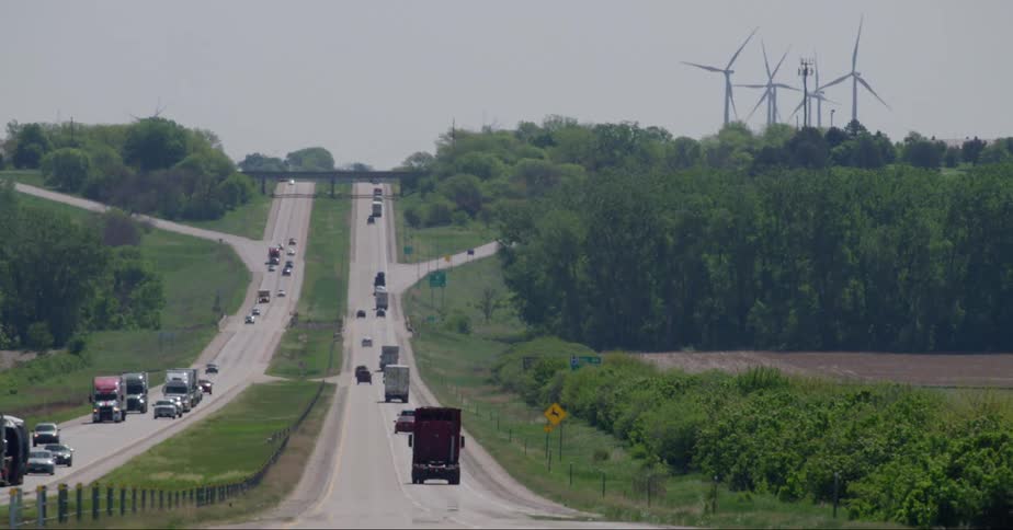 Traffic is driving on the highway about to pass some wind turbines