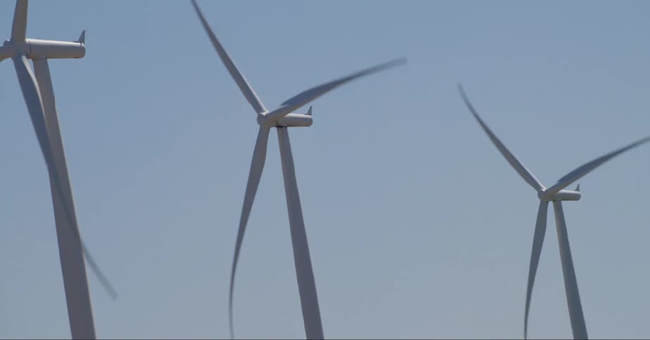 Close up view of wind turbines spinning on a wind farm under a clear sky