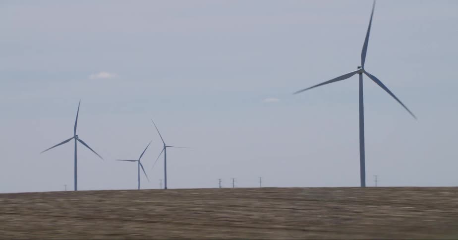 A wind farm is being driven past speedily and shows some windmills in the flat grassland