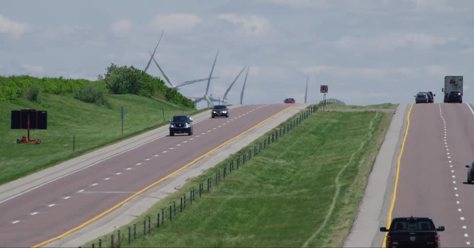View of vehicles traveling on a road with wind energy platforms in the background