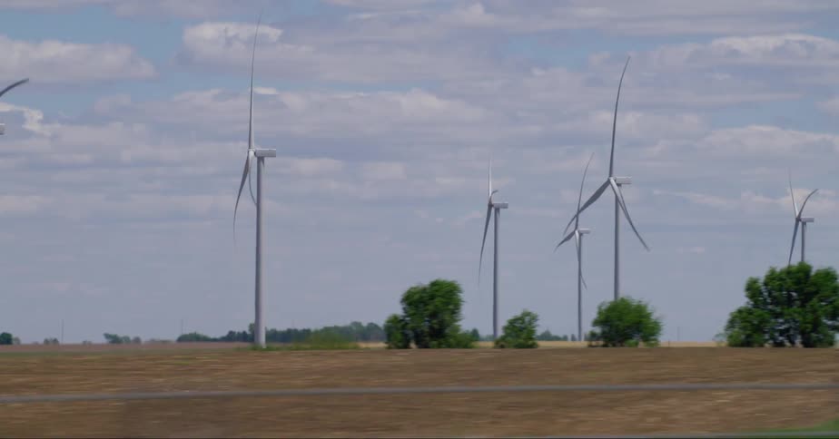 Windmills on a field and passing vehicles at midday