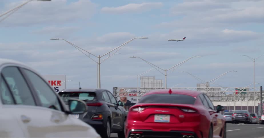 As cars drive down the highway an airplane flies overhead