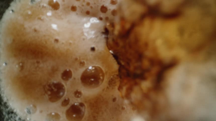 A colalike fluid streams into a bottle we only see into the top of the bottle the fluid includes ice cubes and it fizzes and foams over until all we see is bubbles and foam