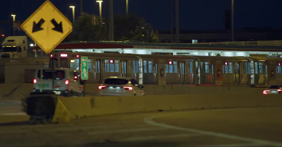 View of a train and personal cars in motion on a road at night