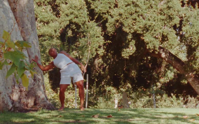 Young woman dancing in the grass next to a tree