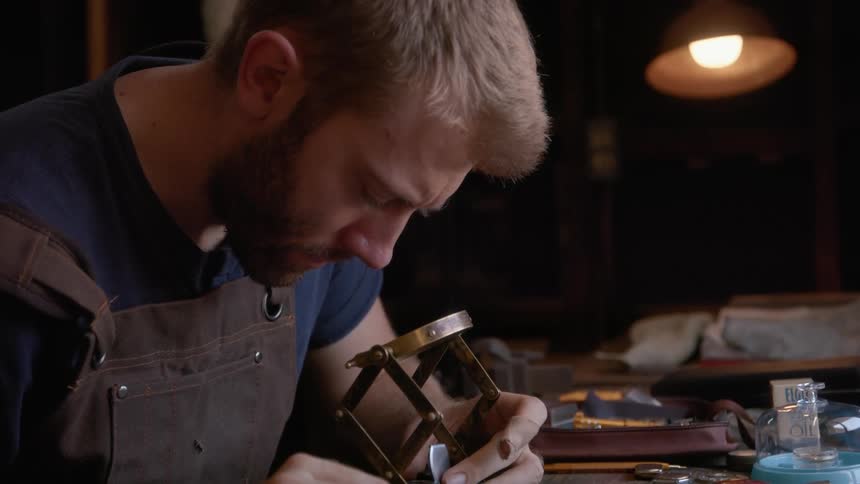 Leatherworker uses a lens to work on a piece over his workbench