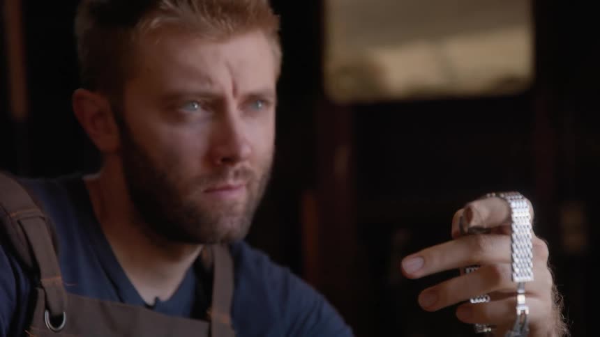 A man is holding and looking at a silver wristwatch