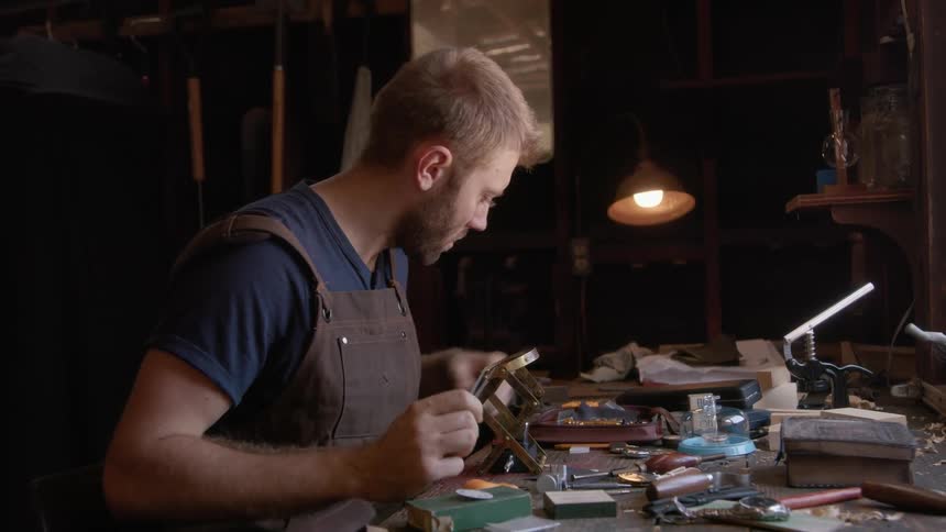A blond man in overalls is arranging a clock on a table