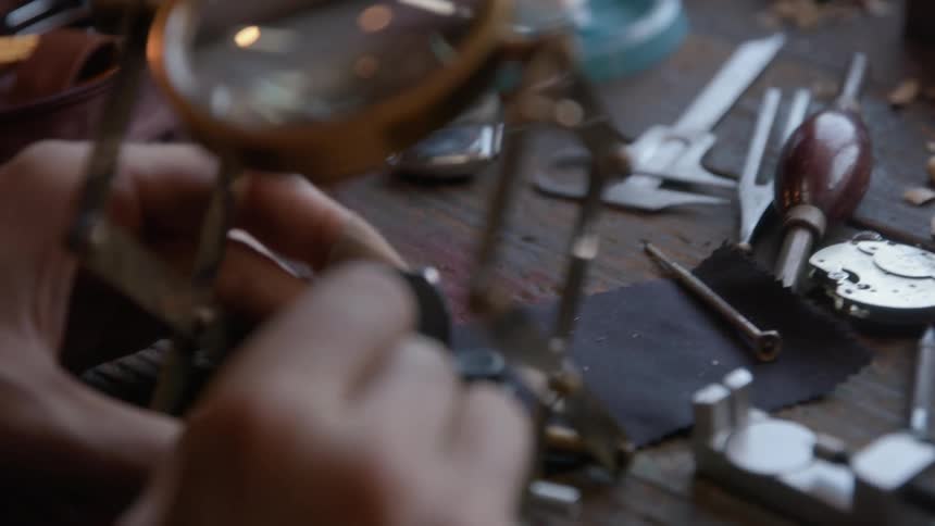 A male watchmaker carefully uses tools while repairing a watch
