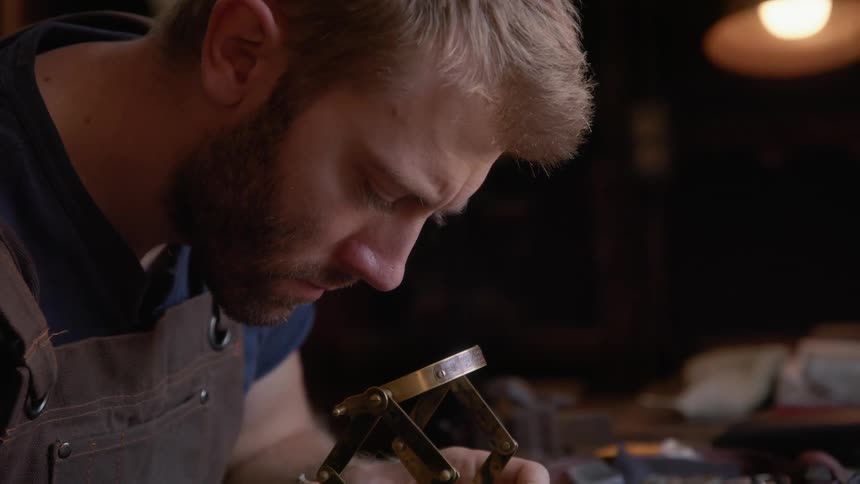 Crafter sits at workbench looking at parts through a magnifying lens