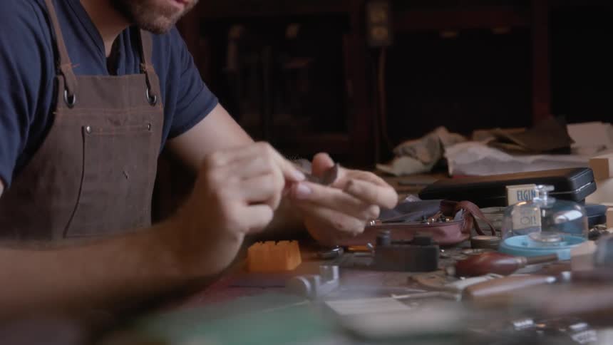 A male watchmaker inspects a part hes holing in his hands