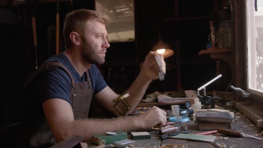 A man is examining a watch on his bench