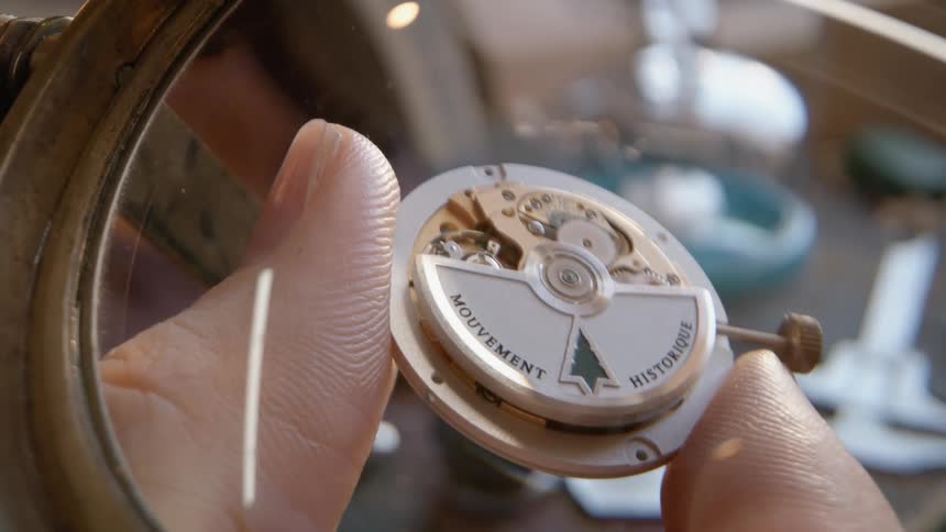 Person examines watch part under a magnifying lens