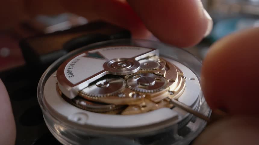 A male watchmaker carefully places the face plate back onto a wristwatch
