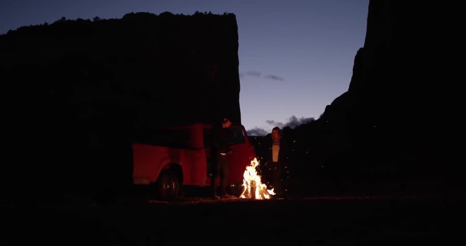 A truck and people are near a fire at dawn