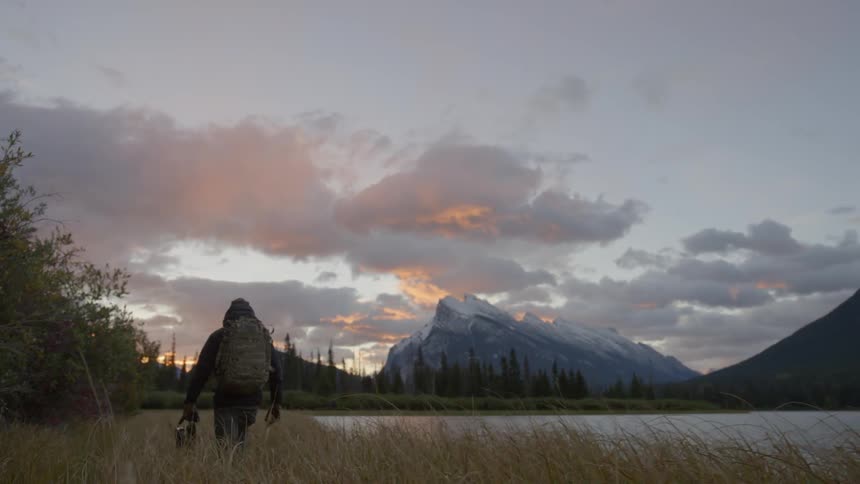 A man is hiking along the side of a lake at dawn