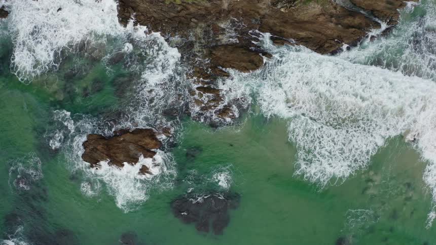 An aerial view of ocean waves crashing against rocks