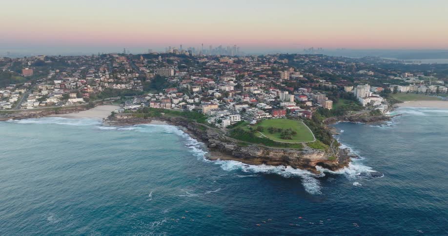 An aerial view of an urban city by the sea with a reddish sky on the horizon