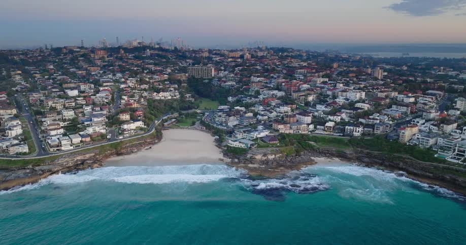 Waves roll onto beach near residential neighborhoods a distance from skyline under a red sky