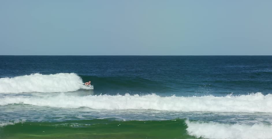 A surfer lies on his surfboard and rides a wave into shore
