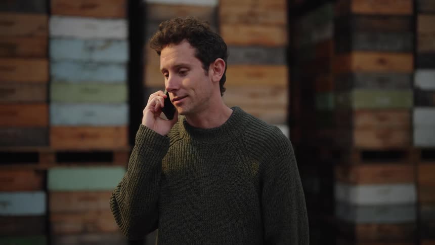 Man with gray sweater talks on the smartphone at the warehouse
