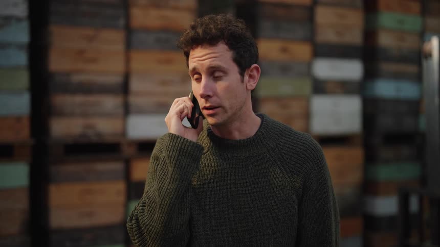 A man stands in front of stacked boxes talking worriedly on a smartphone