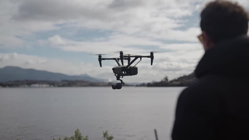 Man directs drone with camera hovering at edge of lake on a cloudy day