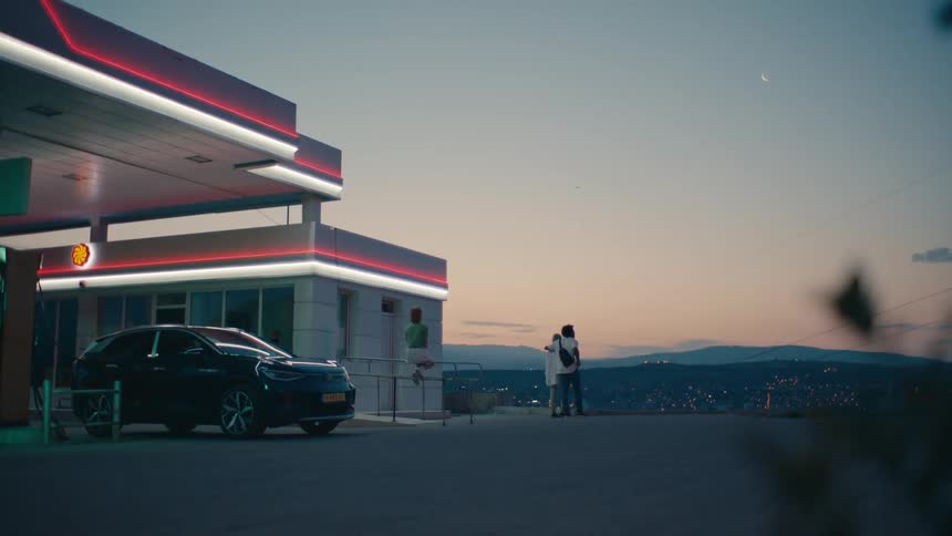 A car parked at a gas station with a couple in front observing the city view during a late afternoon