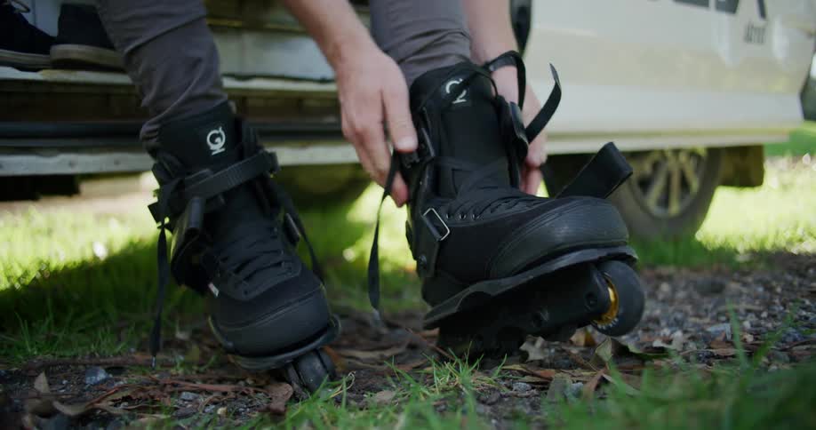 A man sits outside lacing up black rollerblades