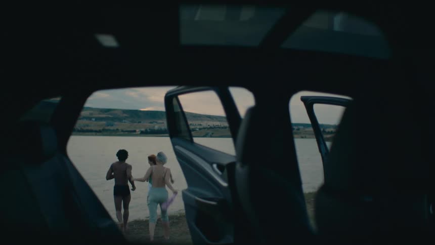 Friends run from car to water while removing their outer layers of clothes