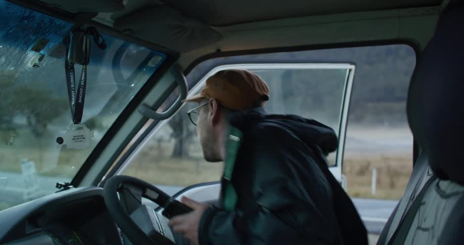 A man gets in a truck parked along a rural road and uses his phone as he sits in the drivers seat