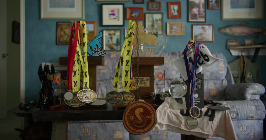 Multiple trophies and medals occupy table in living room