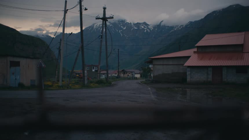 A car passes down a street in a rural town and then some cows cross the street