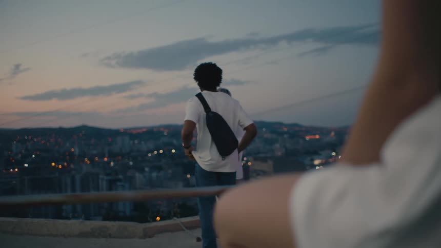 Woman watches man approach another woman looking out onto city scape at dusk