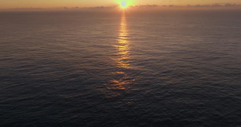 A view of the ocean with the sun on the horizon casting its reflection on the sea