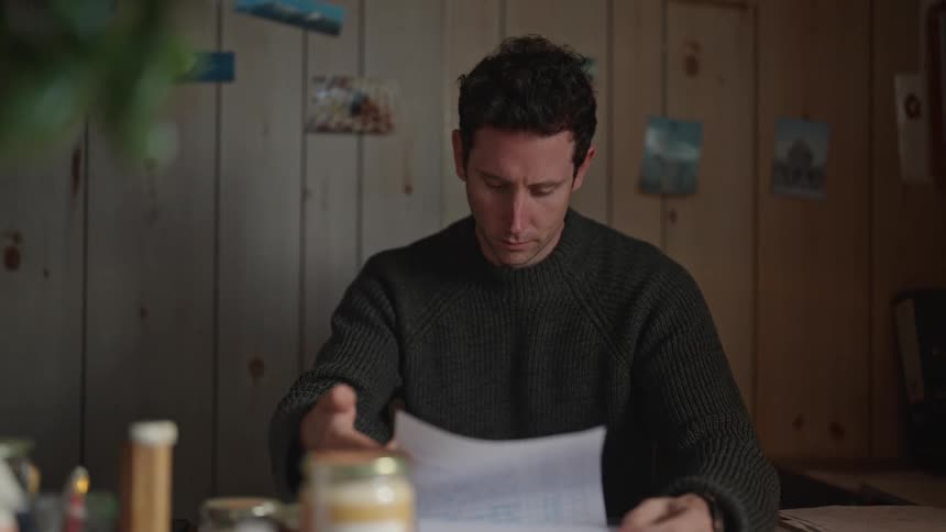 A man is sitting at a table looking at paperwork as he stops and rests his face on his hand
