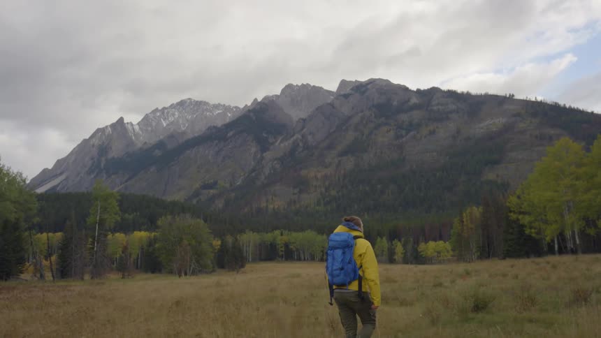 A man is hiking along a long field before a mountain