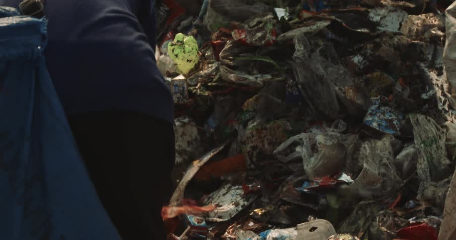 A man uses a large metal hook tool to sift through a massive heap of garbage
