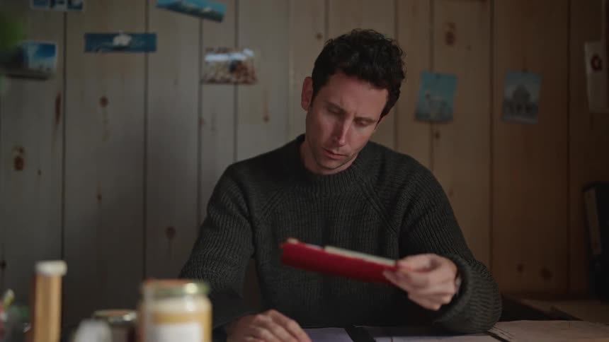 Man sits at table indoors and glances down at clipboard and papers
