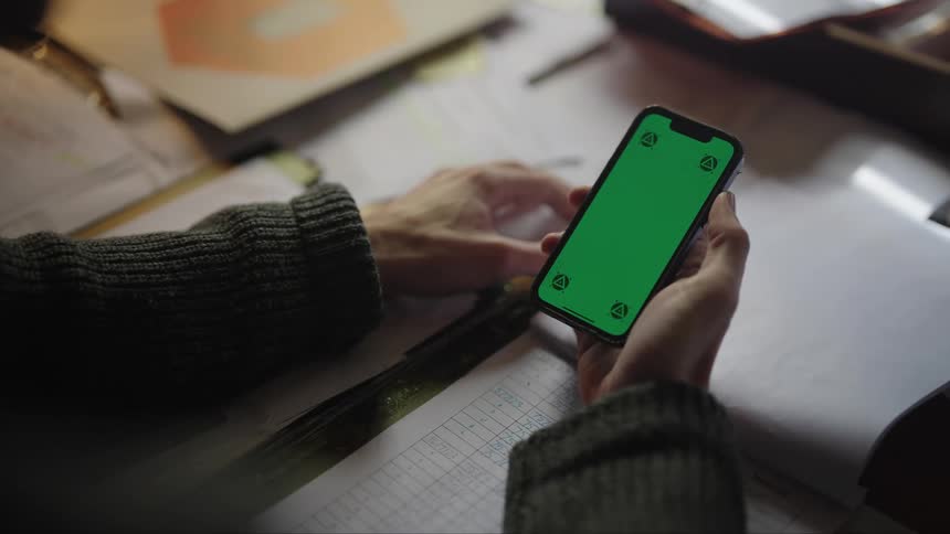 A man is holding a phone and moving his thumb across the green screen