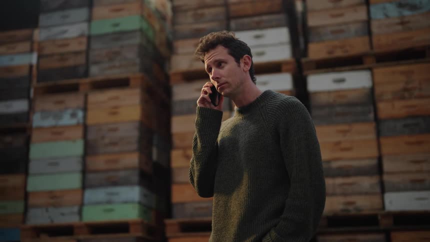 Man with gray sweater talks on the smartphone at the warehouse