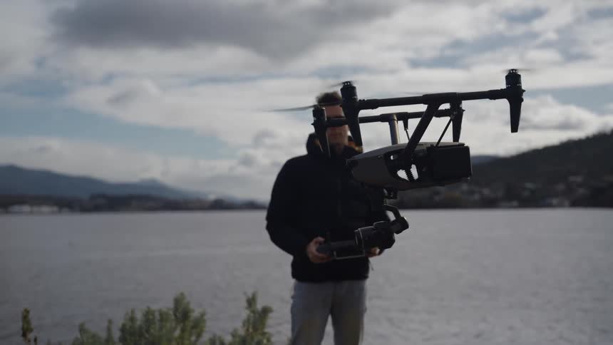 Man flies a drone over a river at sunset